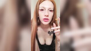 smoking redhead with bright makeup in a black leather dress
